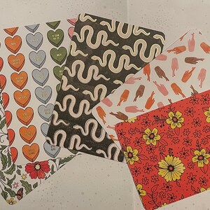 May include: Five different patterned cards with various designs. The cards feature a floral pattern, a snake pattern, a heart pattern, a hand pattern, and a floral pattern with yellow flowers on a red background.