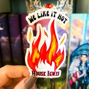 May include: A white sticker with a red and yellow flame design. The sticker says "We Like It Hot" in a black, bold font and "House Ignis" in a black, bold font.