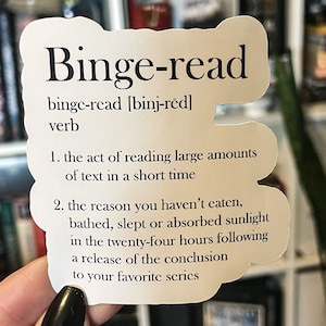 May include: A white sticker with a definition of the word "binge-read". The definition is: "the act of reading large amounts of text in a short time" and "the reason you haven't eaten, bathed, slept or absorbed sunlight in the twenty-four hours following a release of the conclusion to your favorite series".