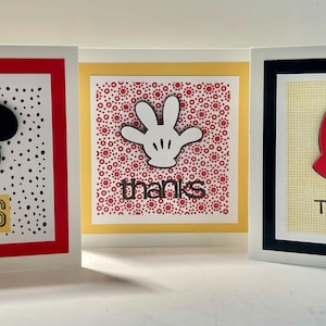 May include: Three thank you cards with a Mickey Mouse theme. The first card has a black silhouette of Mickey Mouse's head on a white background with black polka dots. The second card has a white silhouette of Mickey Mouse's glove on a red background with white polka dots. The third card has a red silhouette of Mickey Mouse's shorts on a yellow background with a white grid pattern. All three cards have a black border and the word "THANKS" printed in black.