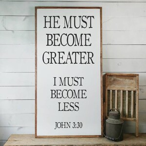 May include: White wooden sign with black text that reads "He must become greater, I must become less, John 3:30".