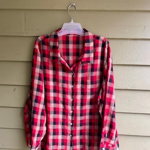 May include: A red, black and cream plaid button-down shirt with long sleeves.