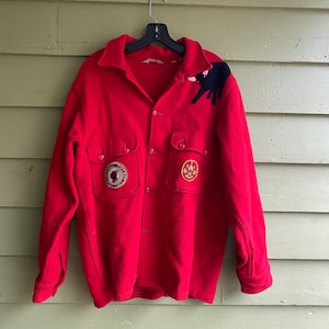 May include: Red wool jacket with a black bear patch on the shoulder and two embroidered patches on the front pockets. The patches are for the Boy Scouts of America.