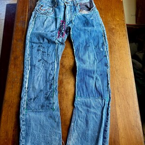 May include: Light blue denim jeans with patches and distressed details. The jeans feature a patchwork design with visible stitching and frayed edges. The jeans have a classic five-pocket design and a button and zipper closure.