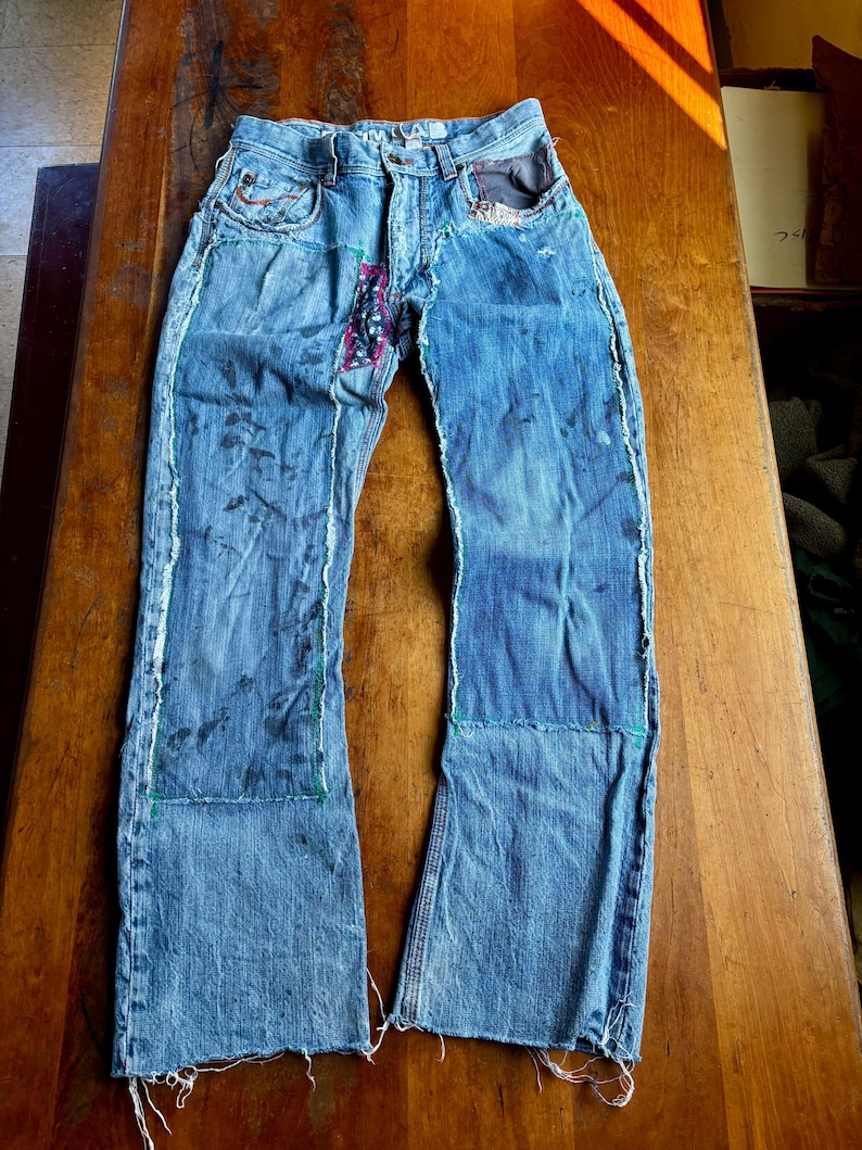 May include: Light blue denim jeans with patches and distressed details. The jeans feature a patchwork design with visible stitching and frayed edges. The jeans have a classic five-pocket design and a button and zipper closure.