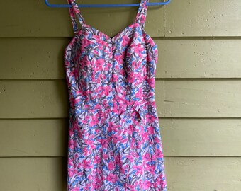 Può includere: Un costume da bagno vintage con stampa floreale, scollo a cuore e spalline regolabili. Il costume da bagno presenta un motivo floreale rosa e blu su sfondo bianco.