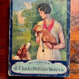 May include: Vintage catalog cover featuring a woman holding a small dog, with another dog looking up at her. The cover has a blue border and text that reads "Your Bargain Book" and "The Charles William Stores, Inc."