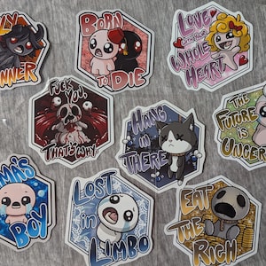 May include: A collection of colorful, die-cut stickers with cartoon illustrations and text. The stickers feature various characters and phrases, including "Only a Sinner," "Born to Die," and "Eat the Rich." The stickers are in various colors and shapes.