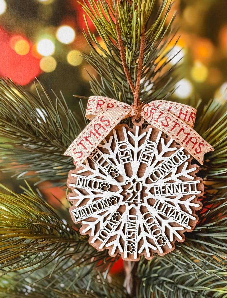 Może przedstawiać: Drewniana ozdoba świąteczna w kształcie płatka śniegu z imionami i odciskami łap, zawieszona na choince. Ozdoba ma rok 2024 i słowo "Christmas" na wstążce. Imiona to Bella, Nico, Josh, Jenn, Connor, Bennett, Madison, Lola, Daisy, Coco i Juliana.