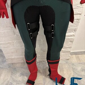 May include: A costume featuring green and black leggings with black accents and red boots. The leggings have a textured pattern and black straps. The red boots have black trim and a strap. The costume is likely for cosplay or a themed event.