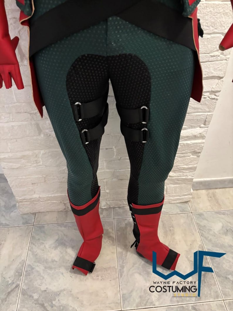 May include: A costume featuring green and black leggings with black accents and red boots. The leggings have a textured pattern and black straps. The red boots have black trim and a strap. The costume is likely for cosplay or a themed event.