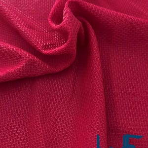 May include: Close-up of a vibrant red fabric with a textured, woven pattern. The material is folded, creating shadows and highlighting the intricate design. The fabric appears to be a synthetic material, possibly for clothing or upholstery.