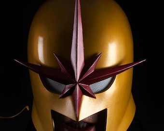 May include: Close-up of a gold and red superhero helmet with a star-shaped design. The helmet has a dark visor and a pointed top.
