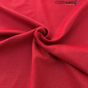 May include: Close-up of a vibrant red fabric with a textured weave. The fabric is draped, showing the interplay of light and shadow. The logo "WAYNE FACTORY COSTUMING STUDIO" is visible in the upper right corner.