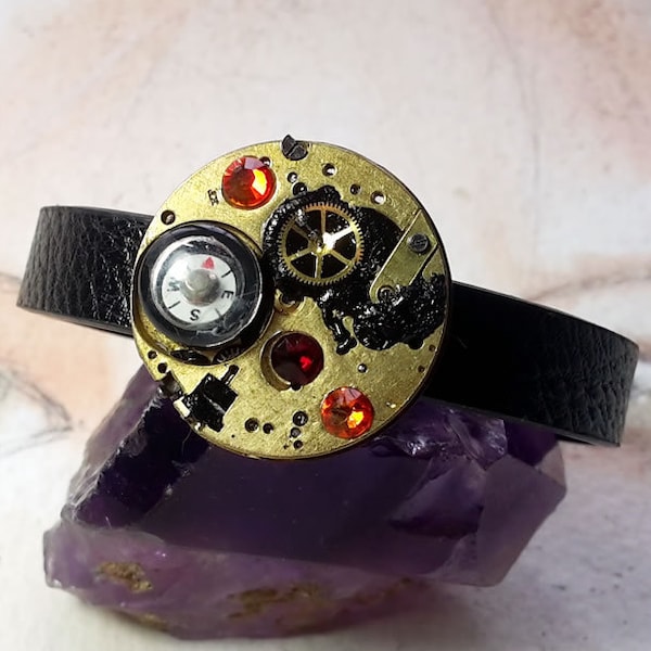 Bracelet Steampunk/Art-déco, lanière noire, pièces de montre laitonnés, résine, boussole, cristaux swarovki rouges, fermoir couleur bronze