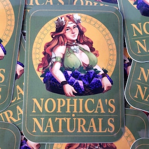 May include: A green sticker with a gold border and the text "NOPHICA'S NATURALS" in gold lettering. A woman with long red hair and a green dress is holding a basket of purple grapes.