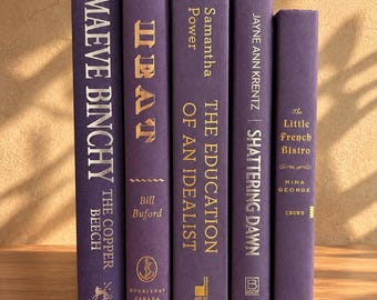 May include: Five hardcover books with purple spines and gold lettering standing upright. The titles include The Copper Beech by Maeve Binchy, Heat by Bill Buford, The Education of an Idealist by Samantha Power, Shattering Dawn by Jayne Ann Krentz, and The Little French Bistro by Nina George.