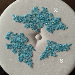 May include: Three turquoise lace appliques with rhinestones, labeled 'XL', 'L', and 'S'.
