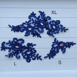 May include: Four navy blue lace appliques in sizes XL, L, and S, with floral and leaf designs. Each applique features iridescent rhinestones and small, dark blue beads. The appliques are displayed on a white, wood-grain surface.