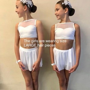 May include: Two girls wearing white dance outfits with white mesh tops and white shorts. They are both wearing white hair pieces with lace details. The girls are wearing size LARGE hair pieces.