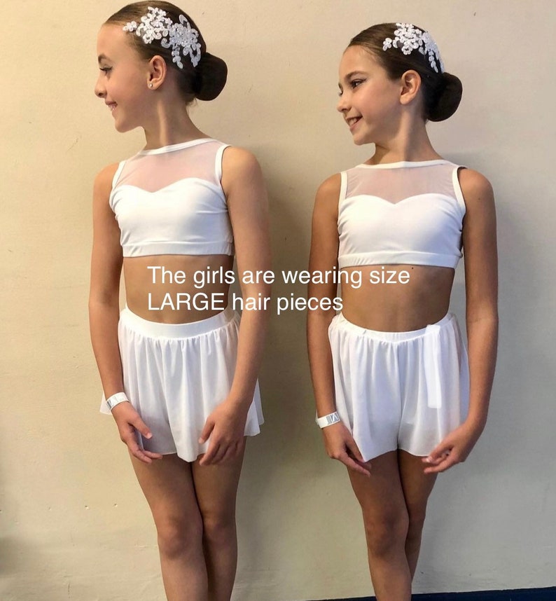 May include: Two girls wearing white dance outfits with white mesh tops and white shorts. They are both wearing white hair pieces with lace details. The girls are wearing size LARGE hair pieces.