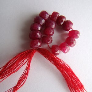 Peut inclure: Un brin de perles de pierres précieuses facettées rouge rubis avec un pompon rouge à chaque extrémité.