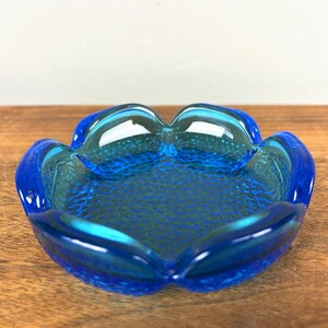 May include: A vibrant blue glass ashtray with a unique, petal-like shape. The ashtray features a textured interior and smooth, rounded edges. The color is a deep, rich blue, adding a touch of elegance to any space.