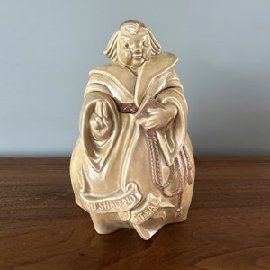 May include: A ceramic cookie jar shaped like a monk with a brown glaze. The monk is wearing a robe and holding a book. The jar has the words "Thou Shalt Not Steal" written on it.
