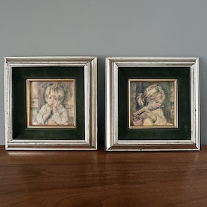 May include: Two framed pictures of children. The picture on the left shows a child with short blonde hair looking down. The picture on the right shows a child with long blonde hair playing a flute.