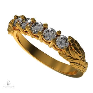 May include: A gold band ring with a row of five clear round diamonds set in prongs. The band is decorated with a leaf design.