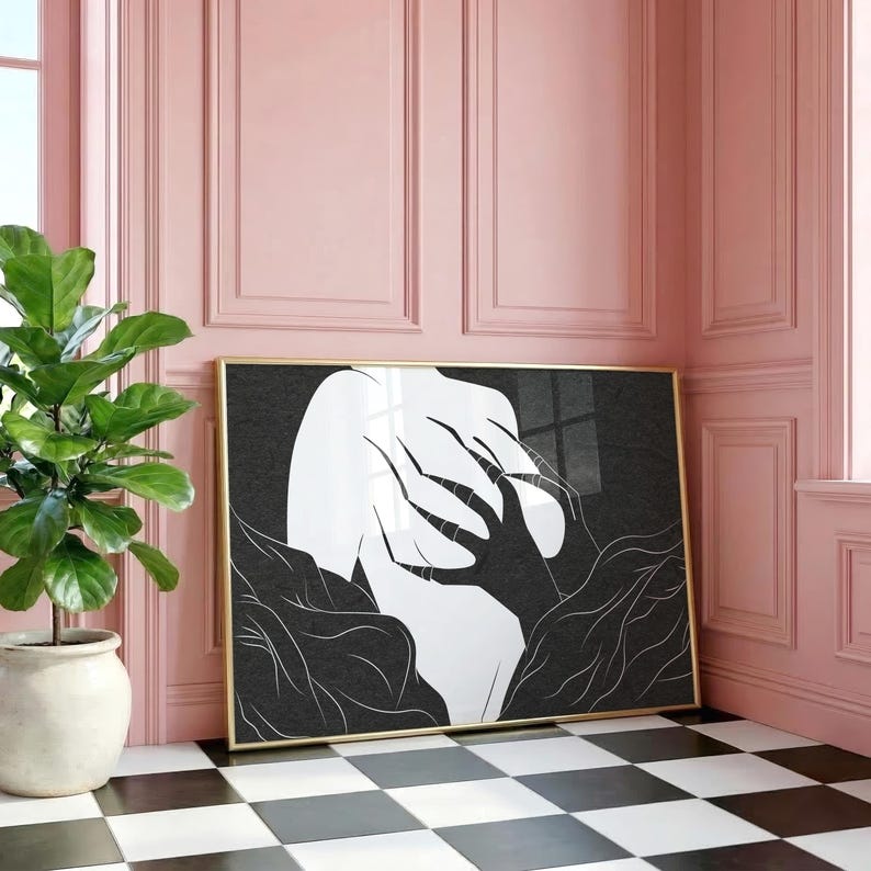 May include: A framed art print featuring a black and white abstract design. The artwork depicts a figure with outstretched hands and surrounding foliage. The frame is gold, and the print is displayed against a pink wall.
