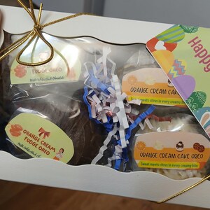 Pu&ograve; includere: Una confezione regalo bianca con una finestra trasparente, contenente biscotti Oreo e torta. I biscotti sono etichettati "Orange Cream Fudge Oreo" e "Fudge Oreo". &Egrave; visibile una carta con "Buona Pasqua".