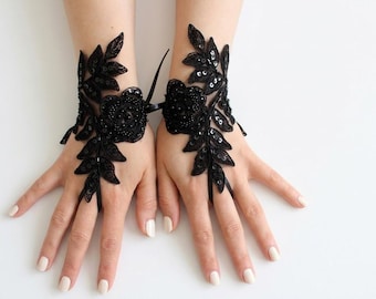 May include: A pair of black lace fingerless gloves featuring intricate floral embroidery, delicate beadwork, and small sequins. The design includes a central rose motif surrounded by leaf patterns, with a thin ribbon loop securing each glove to the middle finger.