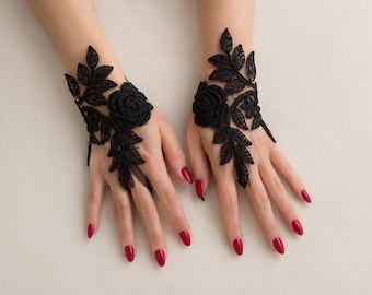 May include: A pair of black lace fingerless gloves featuring intricate floral embroidery with rose motifs and leaf patterns. The delicate lace design covers the back of the hand and extends toward the wrist, secured by a loop around the middle finger.