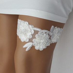 May include: White lace garter with floral embellishments and a delicate design.