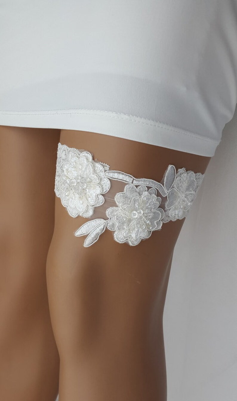 May include: White lace garter with floral embellishments and a delicate design.