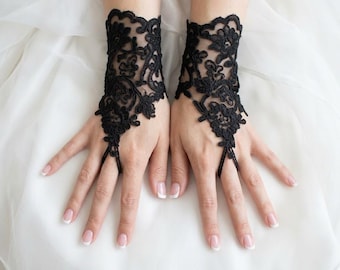 May include: A pair of black lace fingerless gloves featuring an intricate floral embroidery pattern. The gloves cover the wrist and back of the hand, with a delicate loop that secures around the middle finger, leaving the fingers and thumb exposed.
