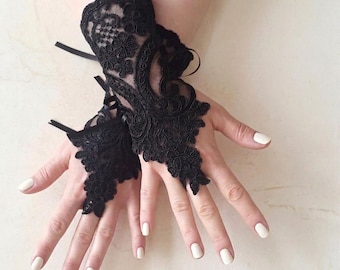 May include: A pair of black lace fingerless gloves featuring intricate floral embroidery and scalloped edges. The gloves are designed to cover the back of the hand and wrist, secured with thin black ribbon ties that extend from the sides.