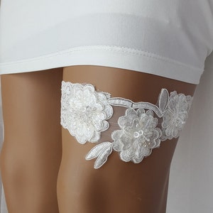May include: White lace garter with floral embellishments and rhinestones.