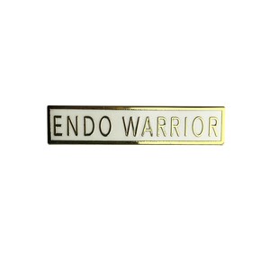 May include: Gold-colored pin with a white background and the text "ENDO WARRIOR" in black.