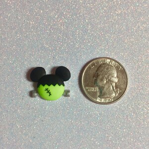May include: Green and black Frankenstein monster charm with a stitched scar on its face. The charm is about the size of a US quarter.