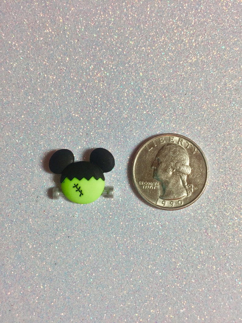 May include: Green and black Frankenstein monster charm with a stitched scar on its face. The charm is about the size of a US quarter.