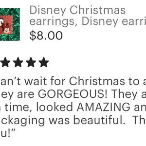 May include: A pair of Christmas-themed earrings featuring Mickey Mouse and Minnie Mouse wearing Santa hats. The earrings are red, black, and white.
