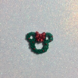 May include: A green Christmas wreath shaped like Mickey Mouse ears with a red bow in the center.