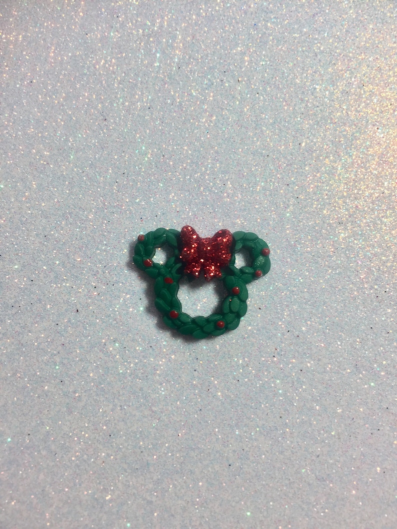 May include: A green Christmas wreath shaped like Mickey Mouse ears with a red bow in the center.