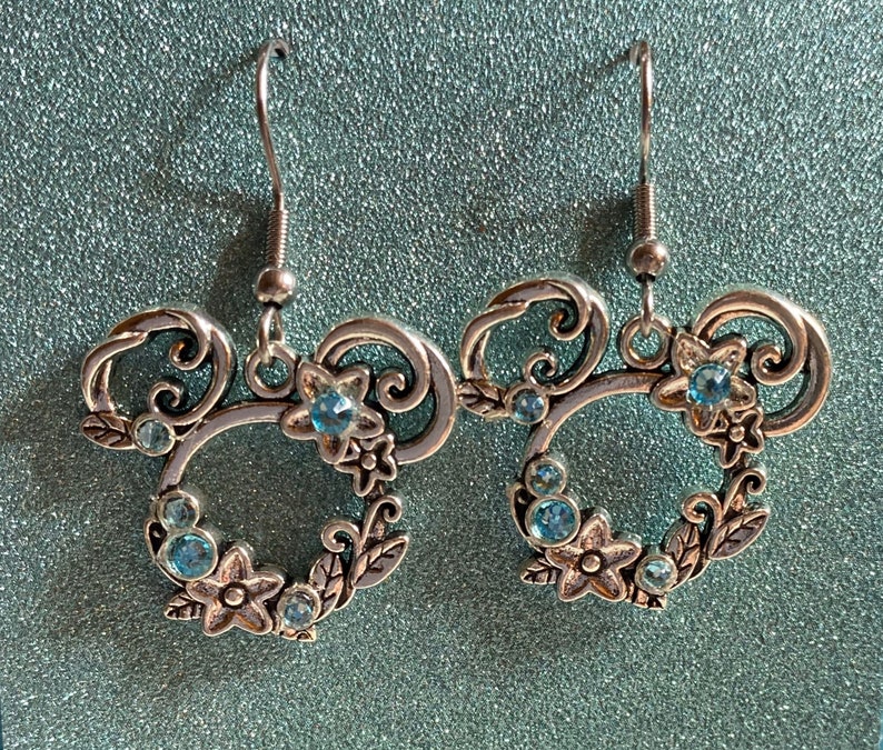 May include: Silver earrings with a floral design and blue rhinestones. The earrings are shaped like a Mickey Mouse head.