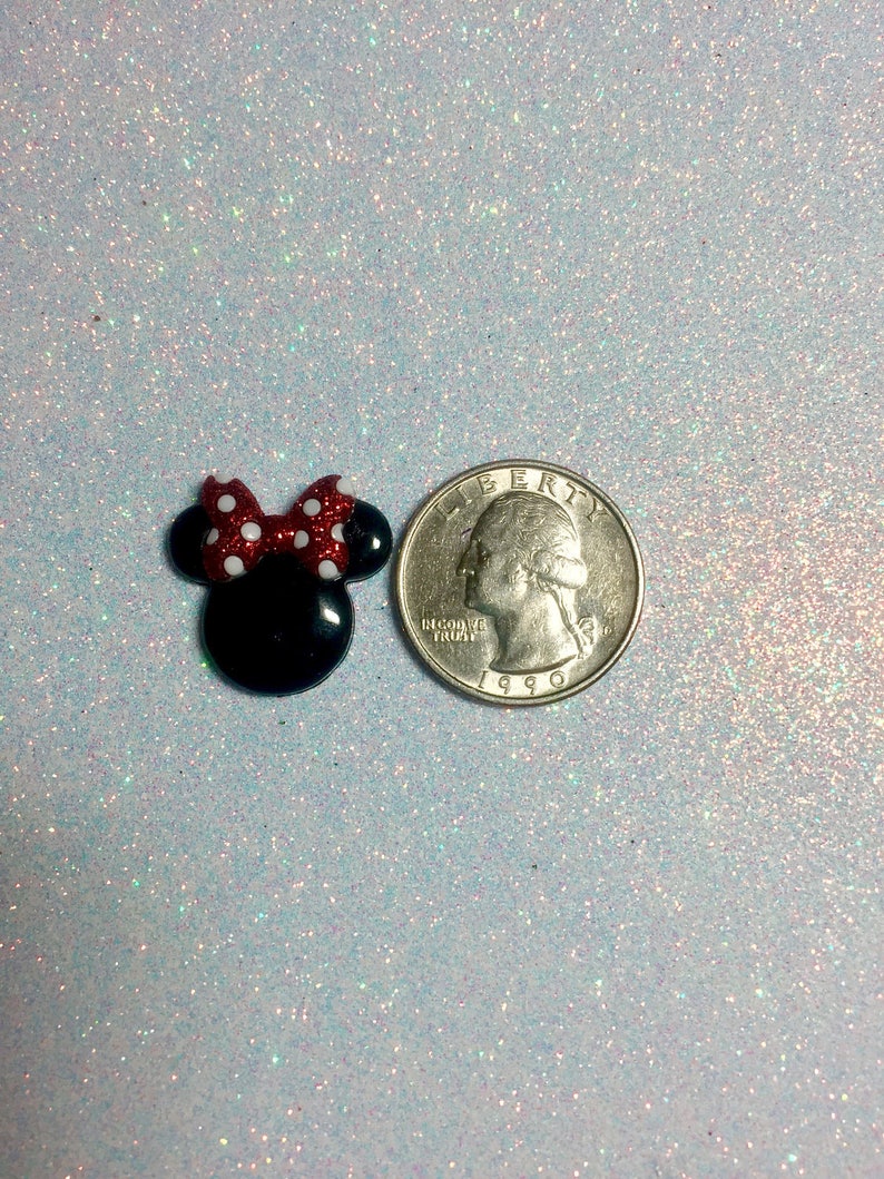 May include: A small black and red Minnie Mouse head with white polka dots. The head is about the size of a US quarter.