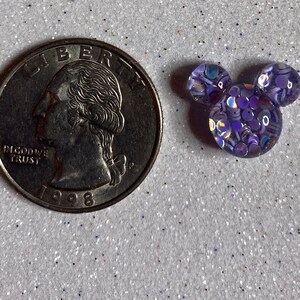 Op de afbeelding: Een kleine paarse en iriserende glitter Mickey Mouse kop charme. De charme is ongeveer de grootte van een Nederlandse 2 euro munt.