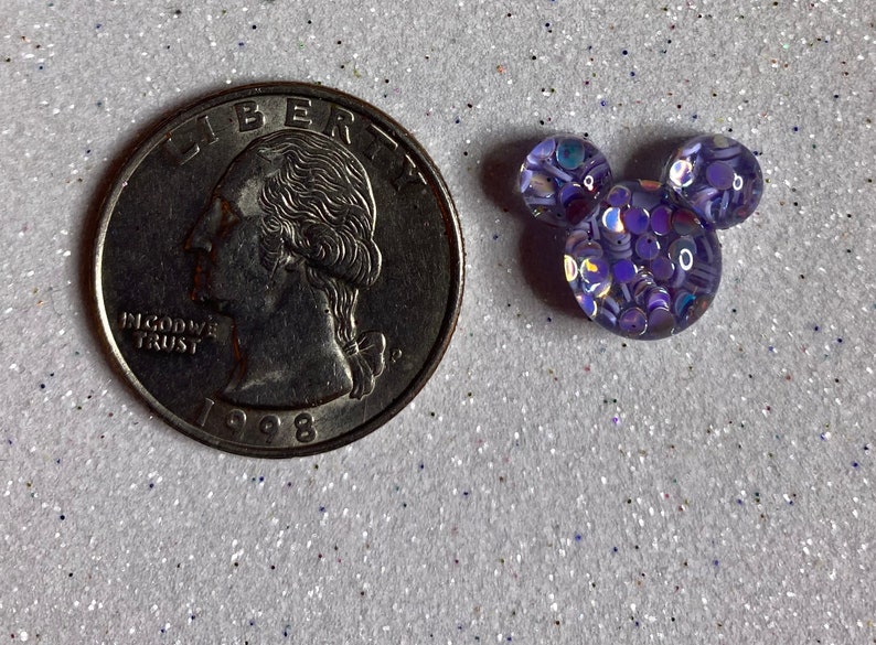 Op de afbeelding: Een kleine paarse en iriserende glitter Mickey Mouse kop charme. De charme is ongeveer de grootte van een Nederlandse 2 euro munt.