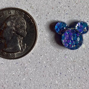 Op de afbeelding: Een blauwe, iriserende Mickey Mouse-kopbedel van hars. De bedel is ongeveer zo groot als een Nederlandse 2 euro munt.